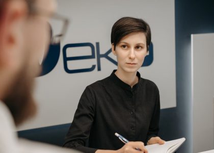 A receptionist at a clinic desk writing notes during a consultation.